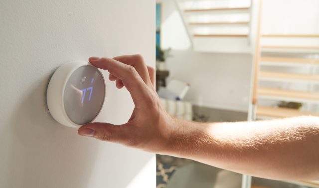 Close Up Of Male Hand Adjusting Digital Central Heating Thermostat In Home