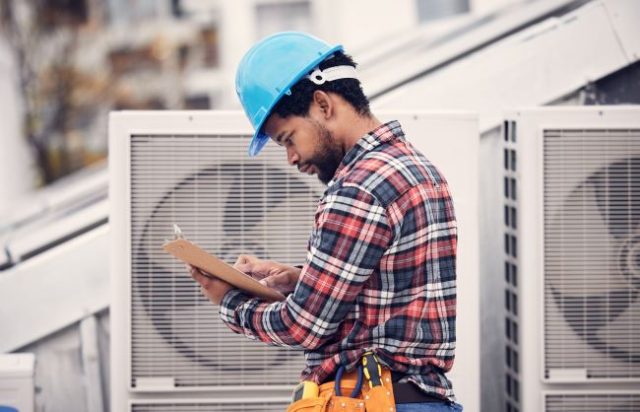 Technician holding clipboard inspecting HVAC system