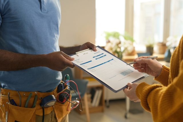 Side view closeup of man with toolbelt handing clipboard to client signing contract