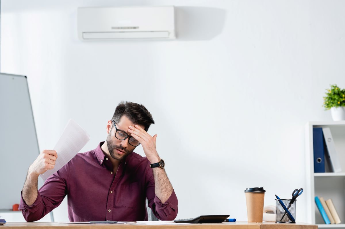 man-waving-paper-while-suffering-from-heat-in-office